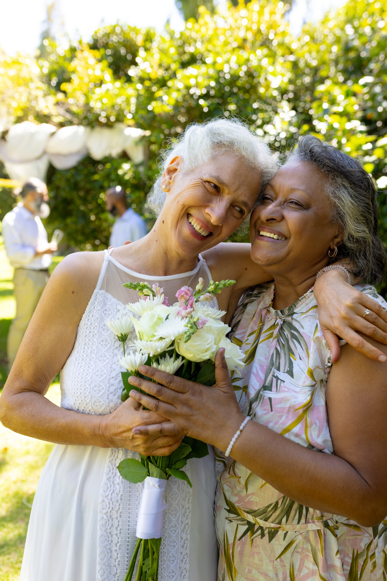 Smiling senior women hugging and holding bouquet of flowers at outdoor event